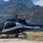 कुमाऊं हेली सेवा से उड़ान भरता हेलिकॉप्टर, पीछे बर्फ से ढके उत्तराखंड के पहाड़