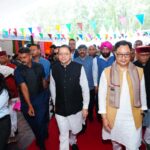 देहरादून के परेड ग्राउंड में लोक संवर्धन पर्व 2026 का उद्घाटन करते मुख्यमंत्री पुष्कर सिंह धामी और केंद्रीय मंत्री किरेन रिजिजू, साथ में पौधरोपण और हस्तशिल्प प्रदर्शनी का अवलोकन।